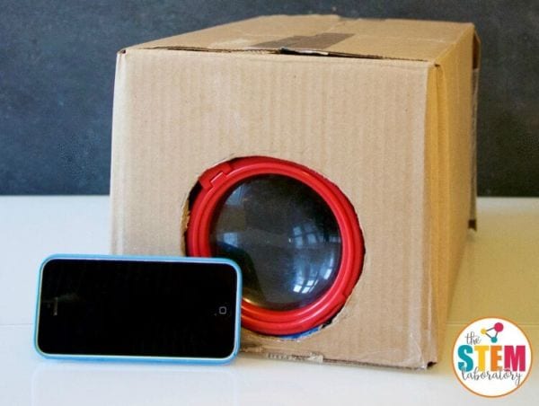 4th Grade Science Experiments Projector STEM Laboratory Cardboard box with a magnifying glass embedded in it, with a smart phone
